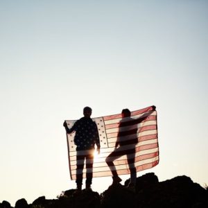 Image of sillouetted people holding a flag on top of a hill